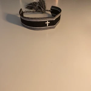 Svart och vitt tygarmband med kors som är hemmagjort!!! - Snyggt svart armband i tyg med vita detaljer och ett broderat kors i mitten. Jag har gjort det ensam hemma!! Med lite hjälp från min mamma… Säljer ett för 110kr och två för 160kr!! Skriv för mer frågor!🙂