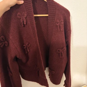 Vinröd kofta med rosetter från bikbok - Superfin vinröd kofta från KC In-progress med stickade rosetter som detalj. Koftan är stickad, har lång ärm och bred ribbad kant framtill. Perfekt för lager-på-lager och ger en mysig vibe till din outfit.