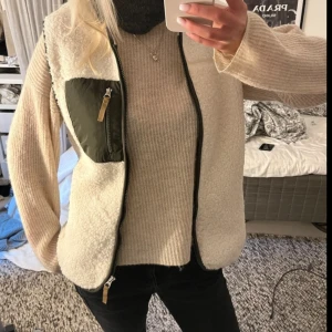 Ljus beige teddyväst - Säljer en beige teddyväst med dragkedja framtill och en snygg grön bröstficka med dragkedja. Västen har svarta detaljer längs kanterna och är perfekt att slänga över en stickad tröja för extra värme. Enkel och stilren design som funkar till många outfits. Storlek xs men passar s-m också, oversized 💗💗 slutsåld!