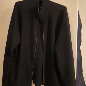 Svart cardigan MASSIMO DUTTI med dragkedja - Svart cardigan tröja från massimo dutti med stilren design och hel dragkedja framtill. Jackan har lång ärm och en rak passform som sitter snyggt på kroppen. Perfekt för dig som gillar minimalistisk stil och vill ha något enkelt att slänga på sig. Materialet känns mjukt och bekvämt.