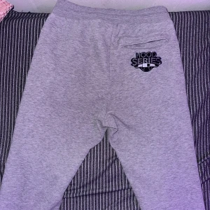 Grå mjukisbyxor från Hoodrich M - Snygga grå mjukisbyxor från Hoodrich i storlek M. Byxorna har broderad Hoodrich-logga framtill och 'Hood Series' bak, elastisk midja och mjukt material. Perfekta för chill dagar och streetwear-stil.