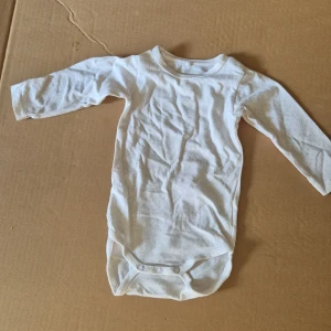 Vit långärmad body från Newborn barn  - Supersöt vit långärmad body från Newborn i mjuk bomull. Små diskreta prickar över hela bodyn och praktiska tryckknappar i grenen. Perfekt för de allra minsta och enkel att matcha med andra plagg.