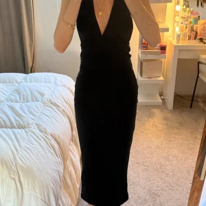 Svart långklänning med öppen rygg - Supersnygg svart långklänning med djup v-ringning och öppen rygg som knyts i nacken och materialet är ribbat. Använd en gång 