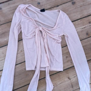 Ljusrosa omlottopp från Gina Tricot - Supersöt ljusrosa omlottopp från Gina Tricot med långa ärmar och knyt framtill. Tunn och mjuk i materialet, perfekt för lager-på-lager eller som statement-piece. Djup v-ringning och croppad passform ger en trendig vibe.