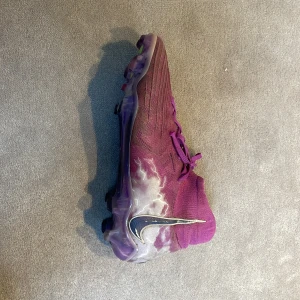Lila Nike fotbollsskor med blixtdetalj - Nypris 3499. Säljer ett par lila Nike Luna fotbollsskor PRO med högt skaft och snörning. Skorna har en cool blixtdesign på sidan och en stor silverfärgad Nike-swoosh. Ovandelen är i syntetmaterial och sulan har dobbar för bra grepp på planen. 