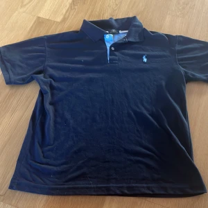 Marinblå Polo Ralph Lauren pike - Klassisk marinblå pike från Polo Ralph Lauren med korta ärmar och krage. Piken har den ikoniska broderade loggan på bröstet och är tillverkad i mjuk bomull. Perfekt för dig som gillar stilren och tidlös design. Storlek M