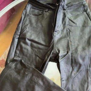 Svarta skinbyxor med rak passform - Snygga svarta skinbyxor med klassisk femficksdesign och dragkedja. Byxorna har en rak passform och är tillverkade i ett mjukt skintyg som passar perfekt till en avslappnad stil.