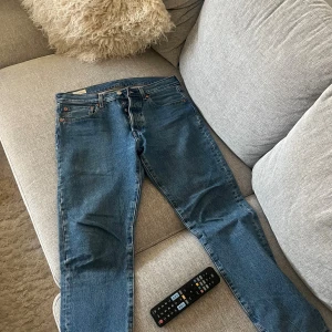 Levi's 501 jeans blå W31 L32 - Klassiska blå Levi's 501 jeans med rak passform och knappgylf. Jeansen har fem fickor, tydliga kontrastsömmar och den ikoniska läderpatchen bak i midjan. Tillverkade i slitstarkt denim med röd Levi's-tag på bakfickan. Perfekta för en avslappnad och tidlös look.