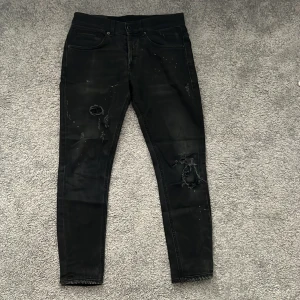 Svarta slim dondup jeans - Svarta slim fit jeans från Dondup med slitna detaljer och hål på benen. Jeansen har fem fickor, låg midja och är tillverkade i stretchig bomullsdenim. Snyggt distressed look med små färgstänk och råa kanter vid knäna. Priset går att diskutera
