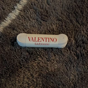 Vita skosnören Valentino Garavani - Vita skosnören från Valentino Garavani, perfekta för att ge dina sneakers eller andra skor en fräsch och exklusiv touch. Klassisk design med Valentino-logga på förpackningen. Passar till flera olika skotyper.