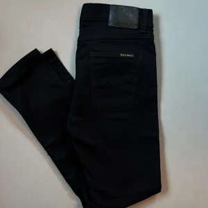 Svarta Nudie Jeans Lean Dean 30/30 - Svarta jeans från Nudie Jeans, modell Lean Dean. Snyggt minimalistisk look med klassisk bakficka och diskret logga. Tillverkade i 99% bomull och 1% elastan för en bekväm passform. Perfekta för dig som gillar stilrena och smala jeans.