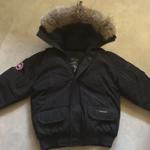 Svart canada goose jacka - Säljer en svart dunjacka från Canada Goose med stor huva och äkta päls runt kanten. Jackan har flera fickor framtill, dragkedja och ribbade muddar. Klassisk patch på ärmen och detaljer i svart. Perfekt för kalla vinterdagar. Jag kan diskutera mer om pris i meddelande!