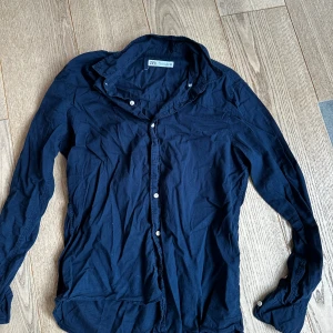 Mörkblå skjorta från Zara - Snygg mörkblå skjorta från Zara i klassisk modell med långa ärmar och knappar framtill. Skjortan är tillverkad i mjuk bomull och passar perfekt till jeans eller chinos. Enkel och stilren design som funkar till många olika looks.