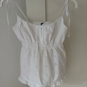 Vit topp med små blommor  - Supersöt vit topp med broderade blommor och tunna axelband som knyts upptill. Den är använd ett fåtal gånger🩷