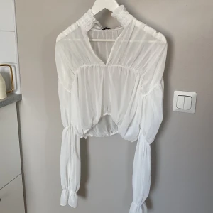 Vit blus med v-ringning från NLY One - Säljer en vit blus från NLY One i storlek S. Blusen har v-ringning, långa puffärmar med resår och knyt vid ärmsluten. Den är croppad och har ett tunt, lätt och flowy material som ger en luftig känsla. 