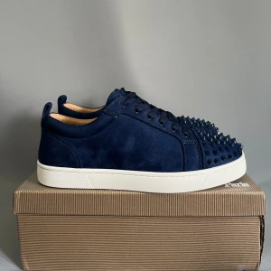 Louboutin sneakers  - Snygga mörkblå sneakers från Louboutin i mocka med coola ton-i-ton nitar över tån. Skorna har vit platt sula och den ikoniska röda undersulan. Perfekta för dig som vill sticka ut med exklusiv streetstyle. Storlek 42 men passar  även 41,43😀