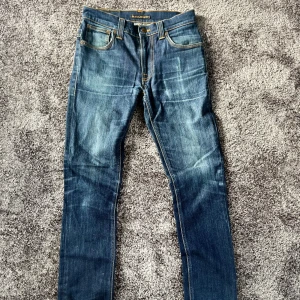Blå  jeans från Nudie Jeans - Säljer ett par stört feta dry jeans från Nudie. Jeansen har en otroligt snygg tvätt och har används under en längre tid. Nypris ca 2000 kr. Mått: midja ca 39cm, ytterbenslängds ca 100cm, benöppning: ca 16cm Hör av er vid minsta lilla fundering!!