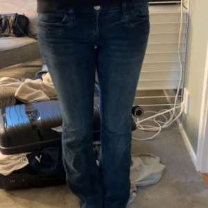 Blå bootcut jeans med breda hällor - Snygga blå jeans med bootcut passform och breda bälteshällor. Jeansen har klassiska fem fickor och en mörk tvätt med lätt slitning. Materialet är jeans och de har en rak men något utsvängd benform som ger en cool siluett.