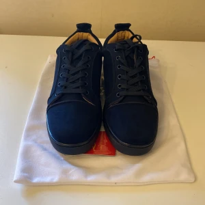 Mörkblå sneakers från Christian Louboutin - Snygga mörkblå sneakers från Christian Louboutin i mocka med klassisk rund tå och platt sula. Skorna har snörning och en stilren design med beige insida. Kommer med originalpåse och äkthetsbevis.