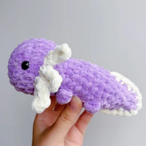 Virkad lila axolotl  - Lila virkad axolotl – handgjord & unik💜🧶 Superfin, mjuk och söt liten axolotl i lila, perfekt som present eller för att ge lite extra charm till hyllan, soffan eller skrivbordet! 	•	Handgjord med kärlek 💜 	•	Virkad i mjukt garn 	•	Ca 17-18cm lång 	•	Unik – bara ett exemplar!  ✨ Pris: 150 kr ✨  Passar både som prydnad och kramdjur 🧸OBS! Dessa innehåller säkerhetsögon som ej är rekommenderade för barn under 3 år!