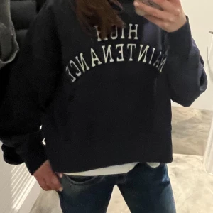 Mörkblå hoodie med tryck - Säljer en mörkblå hoodie med vit texten 'HIGH MAINTENANCE' broderad framtill. Tröjan har huva, magficka och en loose passform. Perfekt för dig som gillar en chill och avslappnad stil. JÄVLIGH COOL och aldrig använd 