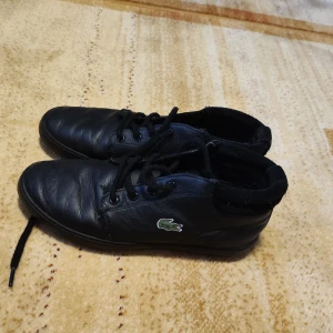 Svarta Lacoste skor  - Lacoste höstskor i äkta läder – nästan nya Stilrena och tidlösa höstskor från Lacoste i äkta svart läder. Lite högre modell som passar perfekt till både vardag och mer dressade outfits. Skorna är i riktigt fint skick och knappt använda – redo för en ny ägare.