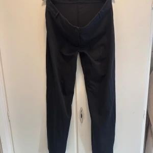 Svarta kostymbyxor med rak passform - Stilrena svarta kostymbyxor från Nelly med klassisk rak passform och diskret knappstängning. Byxorna har bälteshällor och är perfekta för en clean och dressad look. 