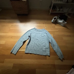 Grå stickad tröja med rund hals - Mysig grå stickad tröja med rund hals och långa ärmar. Tröjan har ribbade muddar vid ärmslut och nederkant, vilket ger en skön passform. Perfekt för kyliga dagar och enkel att matcha med jeans eller kjol.