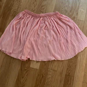 Plisserad rosa kjol från H&M - Supersöt plisserad kjol i ljusrosa från H&M. Kjolen har resår i midjan och ett flowigt, luftigt tyg som ger en riktigt fin siluett. Perfekt för dig som gillar en feminin och lekfull stil.