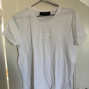 Vit Peak Performance t-shirt - Klassisk vit t-shirt från Peak Performance i storlek M. T-shirten har en diskret logga framtill samt rund halsringning och korta ärmar. Den är tillverkad i mjuk bomull som känns skön mot huden. Perfekt för en clean och stilren look!🥰