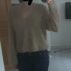 Beige stickad v-ringad tröja  - Mysig beige stickad tröja från ASOS DESIGN med v-ringning och lång ärm. Tröjan har en loose passform och ribbad struktur, perfekt för lager på lager. Enkel att styla till jeans eller kjol för en chill look.