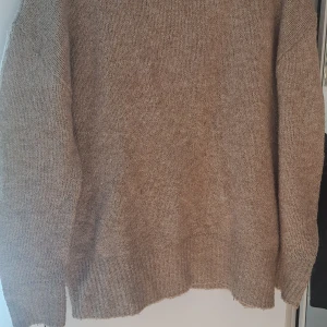Beige stickad tröja med lång ärm - Mysig beige stickad tröja med lång ärm och ribbade muddar vid ärmslut och nederkant. Perfekt för kyliga dagar och enkel att matcha med jeans eller kjol. Neutral färg som passar till det mesta och ger en chill vibe.