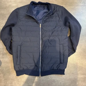 Mörkblå cardigan - Snygg mörkblå cardigan med quiltad framsida och mjuka ärmar. Jackan har hel dragkedja, ståkrage och två sidofickor. Perfekt för dig som vill ha en stilren look nu till hösten Passar dig som gillar mode!