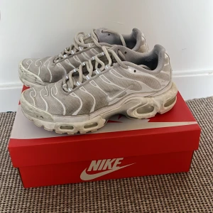 Nike Air Max Plus vita sneakers - Nike Air Max Plus sneakers i vitt med silvriga detaljer och ikoniska Tn-loggan på hälen. Ovandel i mesh och syntet, med synliga Air Max-enheter i sulan för extra komfort. Snyggt vågigt mönster och klassisk snörning. Perfekta för dig som gillar streetwear och sportig stil.