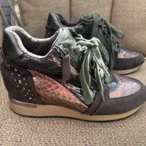 Metallic sneakers med ormskinnsdetaljer - Unika sneakers med metallic roséguld ormskinnsmönster, svart glitter och mörkgrå mockadetaljer. Skorna har gröna snören, dragkedja på sidan och små nitar baktill 