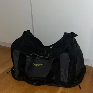 Svart träningsväska  - Stor svart träningsväska från SOC med grå detaljer och limegrönt foder. Väskan har flera fack, dubbla bärhandtag och ett längre. Perfekt för gymmet eller sportaktiviteter, rymmer allt du behöver och är lätt att bära med sig. Finns endast någon liten fläck i ett av facket som inte går bort trots att den blivit tvättad. Säljer då den inte kommer till användning längre 💗