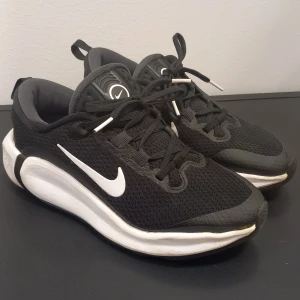 Svarta Nike sneakers med vit sula - Snygga svarta Nike sneakers storlek 36 med vit sula och klassisk vit swoosh på sidan. Ovandelen är i mesh för bra andningsförmåga och skon har snörning framtill. Perfekta för dig som gillar sportig stil och vill ha bekväma skor till vardagen. 