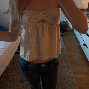 Beige bandeau tubtopp med spetsdetaljer - Säljer en beige bandeau tubtopp med virkad överdel och broderade blommor på den luftiga nederdelen. Toppen är axelbandslös och har en söt spetsdesign som ger en romantisk vibe. Perfekt för varma dagar och sommarhäng.