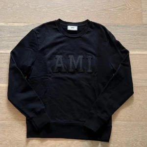 Svart sweatshirt från AMI Paris - Svart sweatshirt från AMI Paris med broderad logga framtill. Tröjan har rund halsringning, ribbade muddar och är tillverkad i mjuk bomull. Perfekt för en chill och stilren look.