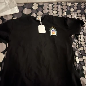 Svart Casablanca t-shirt med tryck - Svart t-shirt från Casablanca med färgglatt tryck av byggnad och nattmotiv på ryggen samt mindre tryck på bröstet. Klassisk passform och rund hals. Perfekt för dig som vill sticka ut med en snygg grafisk tee från ett trendigt märke.