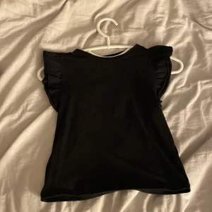 Svart volangärmad topp från 157 - Svart topp från 157 i storlek XS med volangdetaljer på axlarna. Knappt använd och inga skador ! Super fin och passar till allt❣️❣️