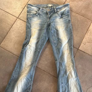 Ljusblå bootcut jeans från Gina young - Snygga ljusblå jeans med bootcut passform och slitna detaljer framtill. Jeansen har klassisk femficksdesign, knapp och dragkedja i gylfen samt coola slitningar längs benen för en trendig look.