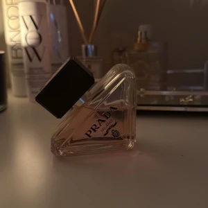 Prada Milano parfym - Säljer en lyxig parfym från Prada Milano i en unik trekantig glasflaska med svart lock. Flaskan har en elegant design och innehåller en ljusrosa doftvätska. Perfekt för dig som vill ha en exklusiv och trendig doft på hyllan. Väldigt sparsamt använd! 