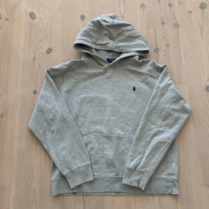 Ralph lauren hoodie - Snygg grå hoodie från Polo Ralph Lauren i storlek S. Klassisk design med huva  och broderad logga på bröstet. Tillverkad i mjuk bomull med ribbade muddar och lång ärm. Perfekt för chill dagar och streetwear vibes.
