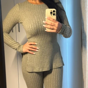 Ribbad grön stickad långärmad tröja med byxor till - Snygg ribbad stickad tröja i en dämpad grön nyans. Tröjan har lång ärm, rund halsringning och slitsar på sidorna för en modern look. Perfekt för lager-på-lager och chill dagar. Passformen är normal och materialet känns mjukt mot huden.