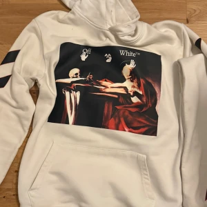 Vit Off-White hoodie med konsttryck - Säljer en vit hoodie från Off-White i 100% bomull med ikoniskt konsttryck framtill och stora pilar med motiv på ryggen. Hoodien har huva, känguruficka och svarta detaljer på ärmarna. Perfekt statement-plagg för dig som gillar streetwear. Storleken på koftan är L men den blev liten p grund av tvättmaskinen. Det kanske passar någon som har storlek S eller någon som är smal. Vi kan snacka om priset om du tycker att det för dyrt.