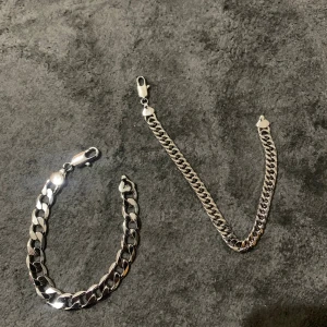 Kedjearmband och halsband i silverfärg - Säljer ett chunky kedjearmband och ett matchande halsband i silverfärgad metall. Båda har platta, breda länkar och robusta karbinlås. Perfekt för dig som gillar stilrena och tuffa accessoarer med lite edge. Snyggt att bära tillsammans eller var för sig.
