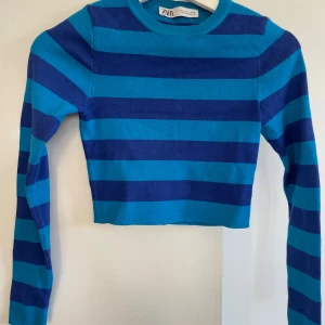 Blå randig croppad tröja från Zara - Säljer en croppad långärmad tröja från Zara i blåa och marinblåa ränder. Tröjan har en tight passform och är tillverkad i en mjuk viskosblandning. Perfekt för dig som gillar färg och vill sticka ut lite extra.