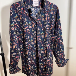 Blommig skjorta från The Seven Seas - Snygg skjorta med blommigt mönster i blått, rött och grönt från The Seven Seas. Skjortan har lång ärm, klassisk krage och knappar framtill. Tillverkad i mjuk bomull som känns skön mot huden. Perfekt för dig som vill sticka ut med färg och mönster.