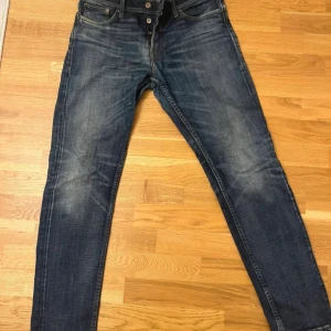 Jack & Jones blå jeans comfort fit - Snygga blå jeans från Jack & Jones med comfort fit och klassisk femficksdesign. Jeansen har knäppning med knappar, kontrastsömmar och en mörk tvätt med slitningar. Perfekta för dig som gillar en avslappnad men stilren look.
